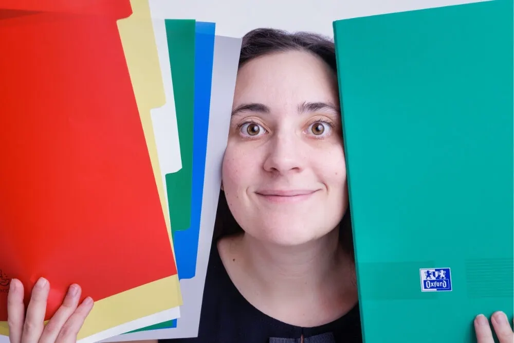 Assistante administrative souriante derrière des classeurs colorés